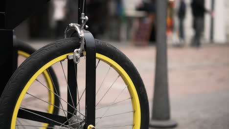 Selective-Focus-Of-Black-and-Yellow-Bicycle-Wheel-Parked-Along-The-Pavement-In-The-City---Low-Angle,-Close-Up-Shot