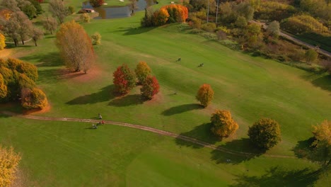 Golf-players-walking-on-beautifully-manicured-grass-in-a-golf-course-in-autumn---panning-aerial-shot