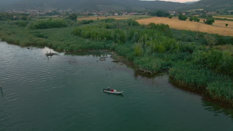 Pescador-En-Un-Bote-De-Madera-A-Orillas-Del-Lago-Con-Exuberantes-Juncos-En-El-Lago-Trasimeno,-Italia