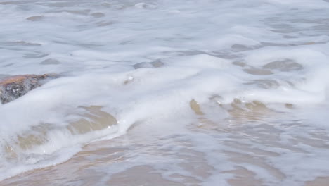Foamy-Waves-Break-Into-Old-Rotten-Wooden-Trunk-On-A-Sunny-Summer-Beach
