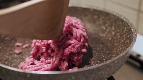 Using-the-Spoon-To-Move-The-Uncooked-Red-Ground-Beef-Into-The-Pan-As-It-Cooks-Over-The-Stove---close-up-view-in-slow-motion
