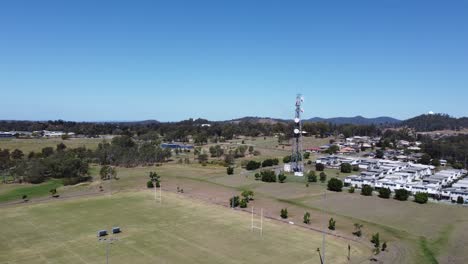 Drone-flying-over-a-football-field-towards-a-Cellphone-tower-in-a-park-and-residential-area