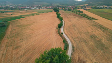 Dirt-Road-Between-Countryside-Fields,-village-and-mountains-in-the-background-In-Magione,-Umbria,-Italy---aerial-shot