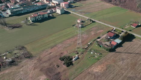 Panoramic-View-Of-Countryside-From-Above-With-Farmers-Fields,-Residential-Houses-And-High-Voltage-Tower-With-Electric-Cables-In-Arcore,-Northern-Italy---aerial-drone,-wide-shot
