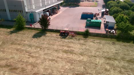 Farmer-On-A-Tractor-Working-On-A-Hay-Field-Near-Industrial-Area---aerial-static-shot