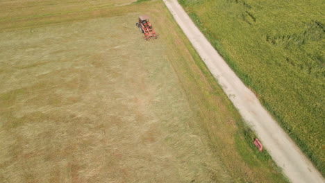 Top-View-Of-A-Working-Tractor-With-Spinning-Mechanical-Rake-On-Freshly-Cut-Hay-Fields-At-Summer-In-Northern-Italy