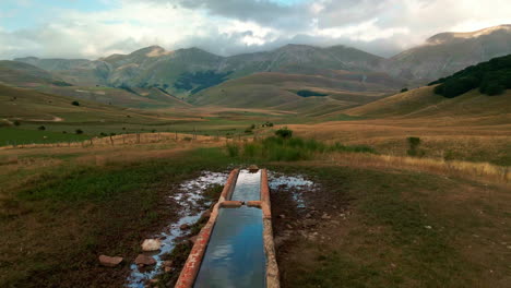 Water-Trough-For-Animal-Livestock-With-Umbria-Valley-In-Distance-During-Sunset-Near-Castelluccio,-Italy