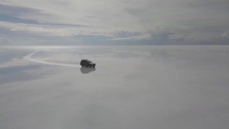 Drone-aerial-shot-of-vehicle-on-salt-flat-Salar-de-Uyuni-in-Bolivia-with-reflection