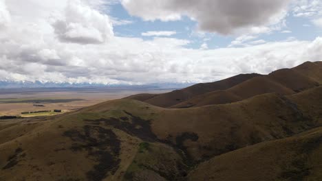 Luftbild---Braune,-Trockene-Kammlinie-In-Neuseeland,-Weite-Ebenen-Und-Schneebedeckte-Berge-Im-Hintergrund