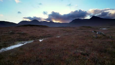 Aerial-drone-footage-flying-low-and-close-to-the-surface-of-a-peat-bogs-towards-dark-mountains-on-the-horizon-at-sunset