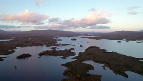 A-drone-slowly-rises-above-a-patchwork-landscape-of-islands-amongst-fresh-water-lochs-and-peat-bogs-at-sunset