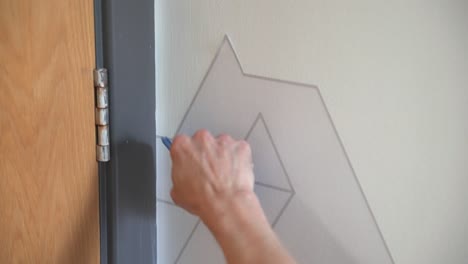 Workman-installing-vinyl-wall-graphic-on-to-wall-for-client-with-geometric-design-using-squeegee-applicator-in-office-space
