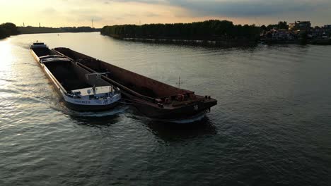 A-cargo-ship-with-side-attached-barge-passing-on-river-at-sunset