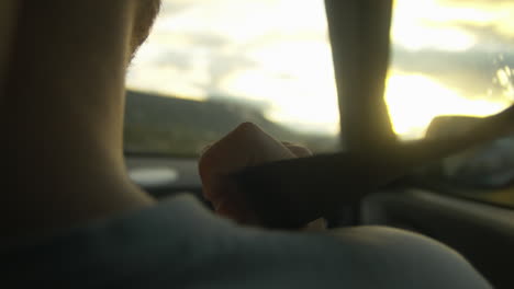 Close-up-seat-belt-on-shoulder-of-man-driving-at-sunset-in-nature