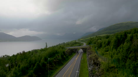 Nordkjosbotn-Tromso-E8-Highway-crossing-verdant-Norwegian-landscape-along-fjord-on-cloudy-day,-Northern-Norway-in-Scandinavia