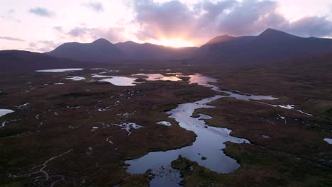 A-drone-slowly-rolls-to-the-left-high-above-a-wetland-landscape-of-islands-and-peat-bogs-surrounded-by-fresh-water-and-looking-towards-mountains-at-sunset