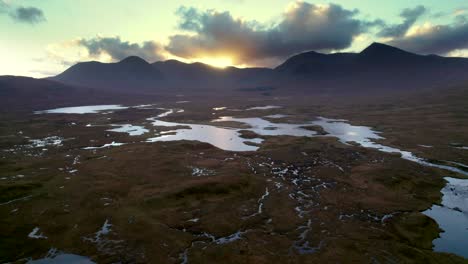 A-drone-slowly-rolls-to-right-left-high-above-a-wetland-landscape-of-islands-and-peat-bogs-surrounded-by-fresh-water-and-looking-towards-mountains-at-sunset