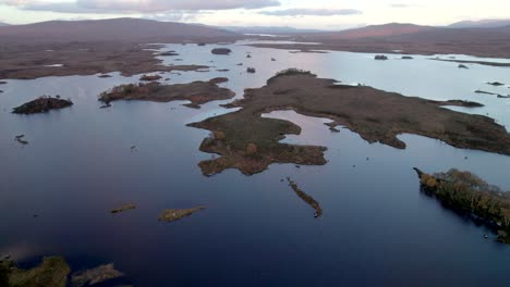 A-drone-slowly-flies-high-above-a-patchwork-landscape-of-islands-dotted-with-trees-and-set-amongst-fresh-water-lochs-and-surrounded-by-peat-bogs-at-sunset