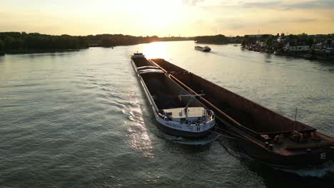 AERIAL---Two-cargo-barges-at-sunset-in-a-river-in-The-Netherlands,-spinning-shot