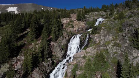 Aerial-View-of-Waterfall-With-Glacial-Water-in-Mountain-Landscape-on-Sunny-Summer-Day