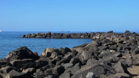 Stone-pier-at-the-beach-of-Playa-De-Las-Americas-,-sunny-summer-day,-calm-Atlantic-ocean-in-the-background,-medium-handheld-shot