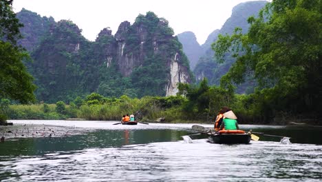 Rowing-Boats-Tours-Taking-Place-Near-Ninh-Binh-For-Tourists-In-Vietnam-With-Limestone-Cliffs-In-Background