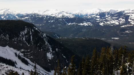 Incredible-reverse-reveal-shot-of-the-beautiful-terrain-of-the-Garibaldi-Provincial-Park-in-the-winter,-snow-covered-Coastal-Mountains-and-evergreen-forests