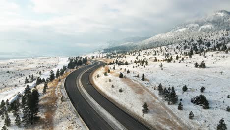 Cars-driving-on-the-Coquihalla-Highway-5-between-Merritt-and-Kamloops-on-a-partly-cloudy-day-in-the-winter,-mountain-sides-covered-in-snow