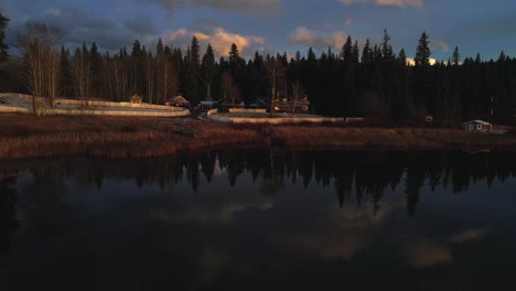 Gorgeous-Approach-Shot-over-Glimpse-Lake-in-British-Columbia,-Canada,-beautiful-reflections-of-the-sky-in-the-water,-golden-hour-light,-fir-forest,-home-ranch