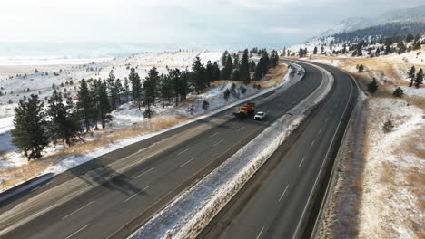 Snow-removal-vehicle-moving-on-the-Coquihalla-Highway-5-between-Merritt-and-Kamloops-on-a-partly-cloudy-day-in-the-winter,-mountain-sides-covered-in-snow
