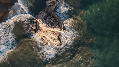 A-top-down-aerial-close-of-the-iconic-Raven-Rock-of-El-Peñón-del-Cuervo-with-the-dark-blue-water-of-the-Alboran-Sea-crashing-in-at-Malaga-Spain