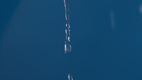 Echter-Reiner-Wassertropfen-Mit-Spritzern-Auf-Blauem-Hintergrund,-Der-In-Zeitlupe-Schießt