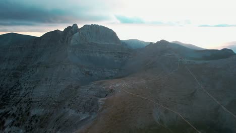 establishing-wide-aerial-shot-of-mountain-Olympus-reveals-a-hut-with-campers-and-tents-on-the-valley-while-the-sun-sets-and-the-clouds-cover-it