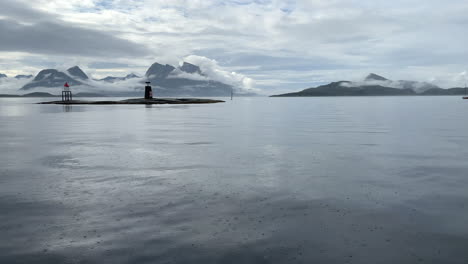 Schwenkaufnahme-Einer-Erstaunlich-Ruhigen-Meereslandschaft-Mit-Wolkenverhangenen-Bergen-Und-Himmel,-Inseln-Und-Leuchtfeuern-An-Der-Küste-Norwegens