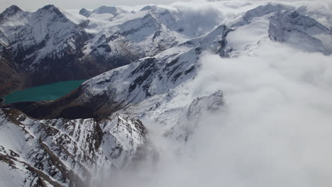 Aerial-birds-eye-flight-over-snowy-mountains-of-Austria-during-cloudy-and-sunny-day---Beautiful-lake-in-the-valley