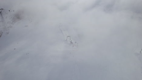 Aerial-top-down-shot-ski-area-with-skier-skiing-snowy-mountain-during-cloudy-and-foggy-day