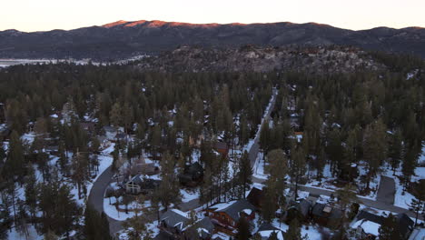 Pan-aerial-Drone-shot-of-residential-in-rural-area-in-winter-and-snow-With-Pine-trees-and-mountains