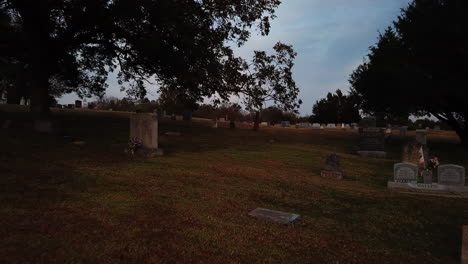 Flying-Low-Over-Peaceful-Green-Field-In-Cemetery,-Green-Trees-All-Around
