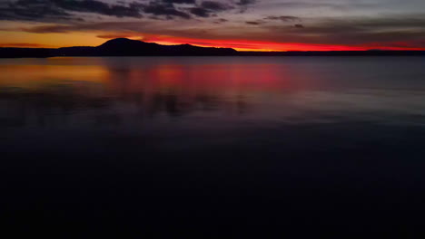 Sonnenuntergangsdämmerung-über-Hügeln,-Aufgenommen-Vom-Rand-Eines-Großen-Sees---Drohnenrutsche-Zu-Ästen---Ozean-Und-Meer-Stockvideos