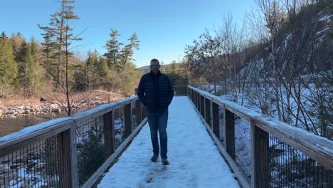 Man-walking-across-a-snowy-bridge-over-a-river-at-winter---slow-motion