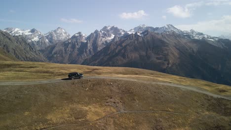 Coche-Negro-Conduciendo-Por-Una-Carretera-Con-La-Montaña-Del-Cáucaso-Al-Fondo,-Svaneti,-Georgia