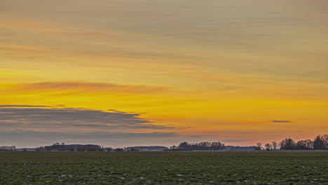 Goldener-Orangefarbener-Sonnenuntergangshimmel-Mit-Wolken,-Die-Von-Links-Nach-Rechts-über-Die-Ländliche-Landschaft-Ziehen