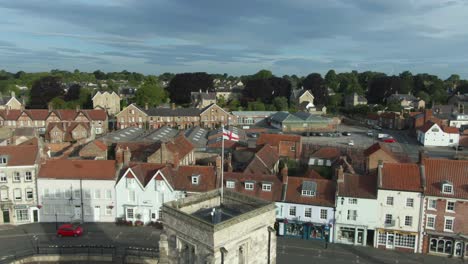 Drone-parallax-around-english-village-market-town-church-with-St-Georges-flag-flying-in-the-wind-on-cloudy-morning