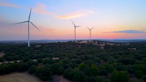 Colorful-wind-turbines'-aerial-sliding-shoot-at-dawn-over-deep-dense-green-forest
