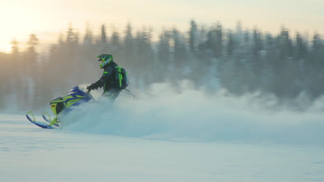 Snowmobile-rider-leaving-snowy-powder-trail-speeding-across-arctic-circle-woodland-at-sunrise