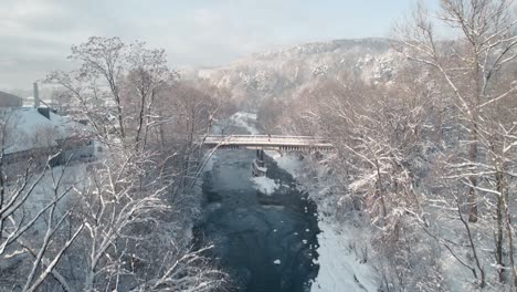 Pequeño-Puente-En-El-Bosque-Cubierto-De-Nieve-Y-Río-Congelado-En-La-Mañana-Helada