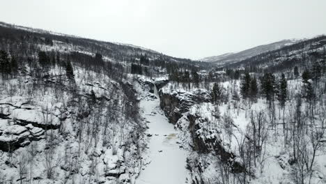 Drone-flight-over-canyon-with-frozen-river-and-falls-in-Norwegian-wilderness
