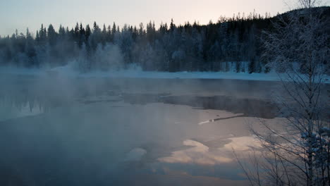 Dreamy-sunrise-frosty-morning-rising-mist-from-cold-alpine-woodland-frozen-lake,-Sweden