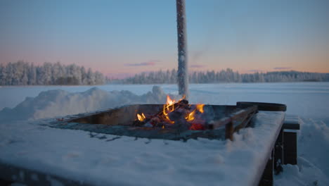 Charred-firewood-logs-burning-in-snowy-frozen-Lapland-outdoor-campfire-stove