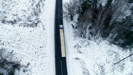 Isolated-long-truck-loaded-with-lumber-driving-slowly-along-snowy-road
